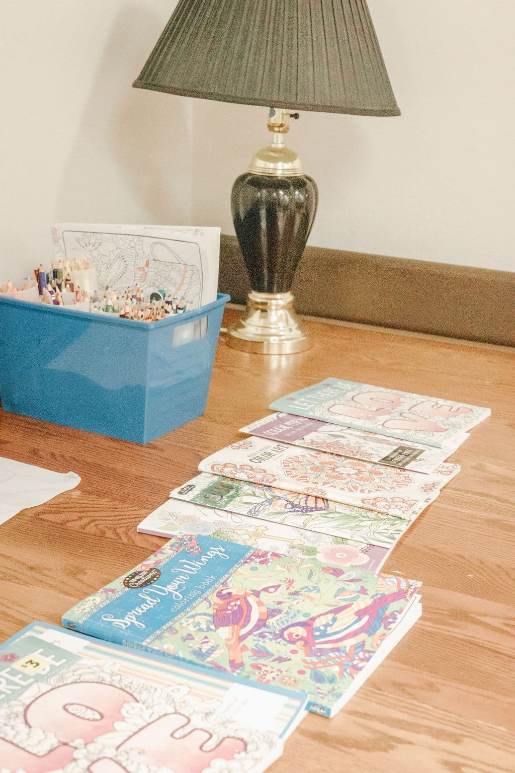 Coloring books fanned across a wooden table at Redwood Park beside a bin of colored pencils and a table lamp