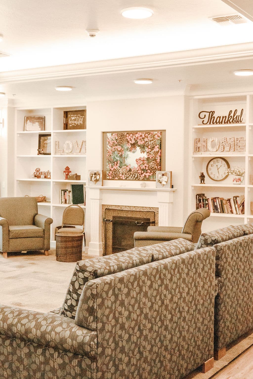 The living room at Oak Grove, with armchairs around a fireplace between built-in bookshelves and a wall clock