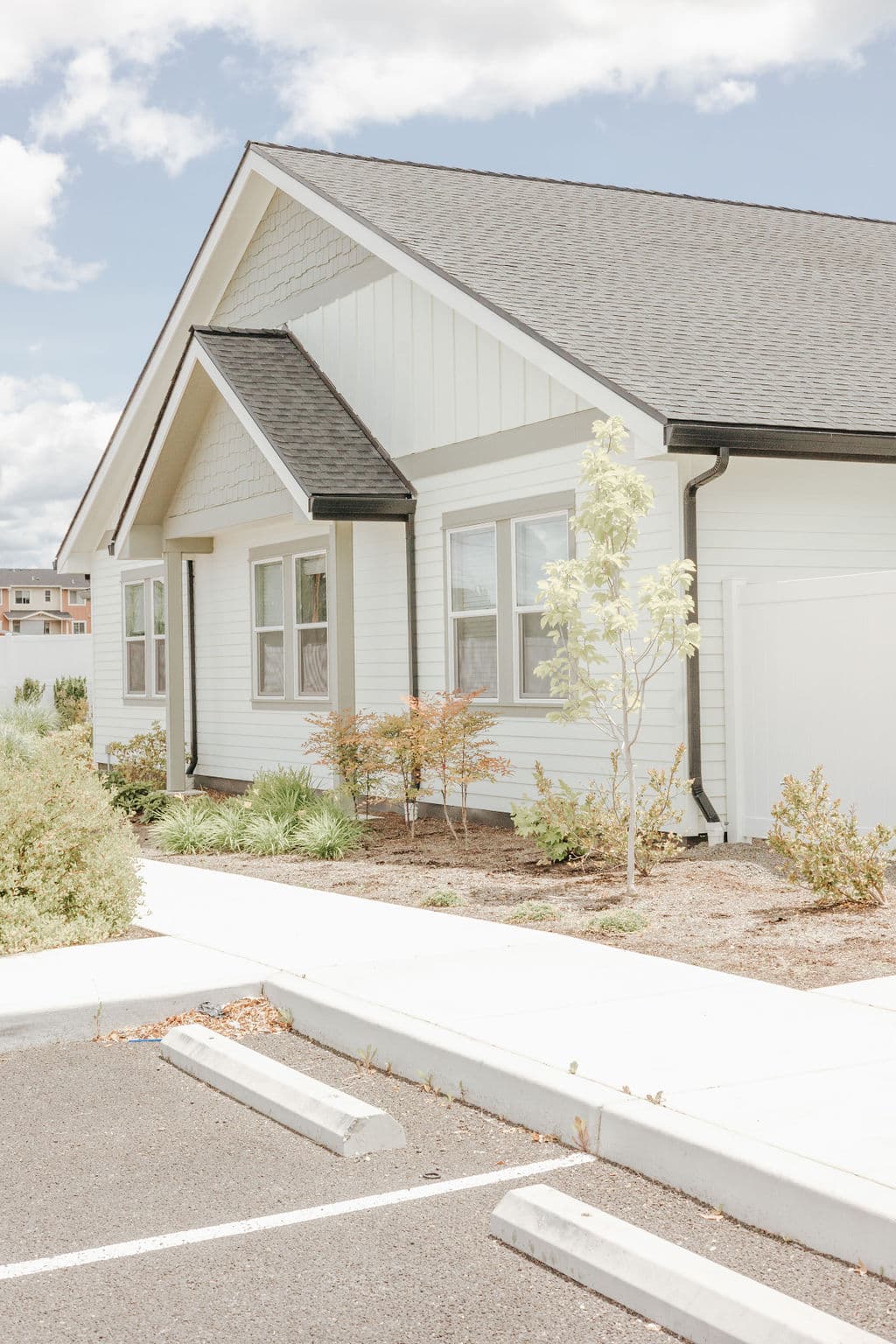 A white cottage at Oak Grove in Medford, with a young tree and landscaped beds along the front walk